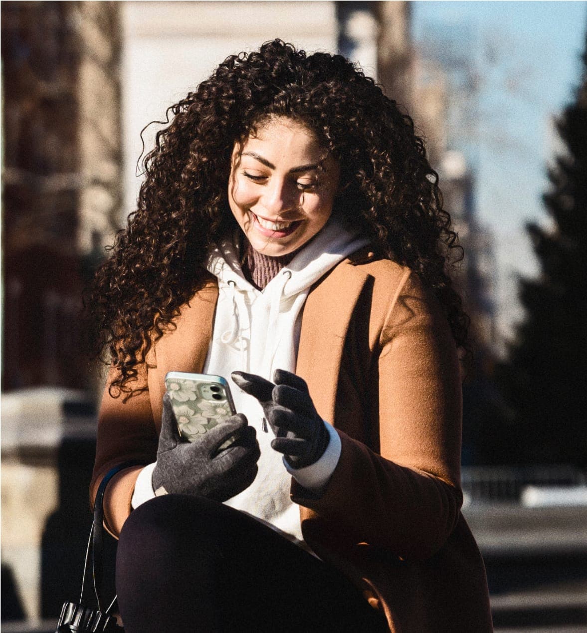 Sample conversational snippet from a student ambassador via Unibuddy overlayed on top of a smiling woman wearing brown coat interacting with phone outside